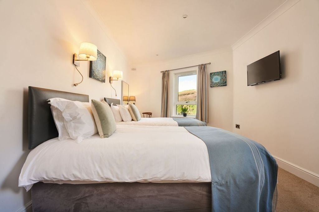 A bedroom with two beds, a TV, and a window with curtains.