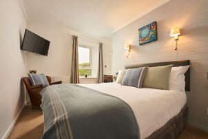 Una habitación de hotel con una cama grande, un televisor montado en la pared, una ventana con cortinas y un cuadro sobre la cama.