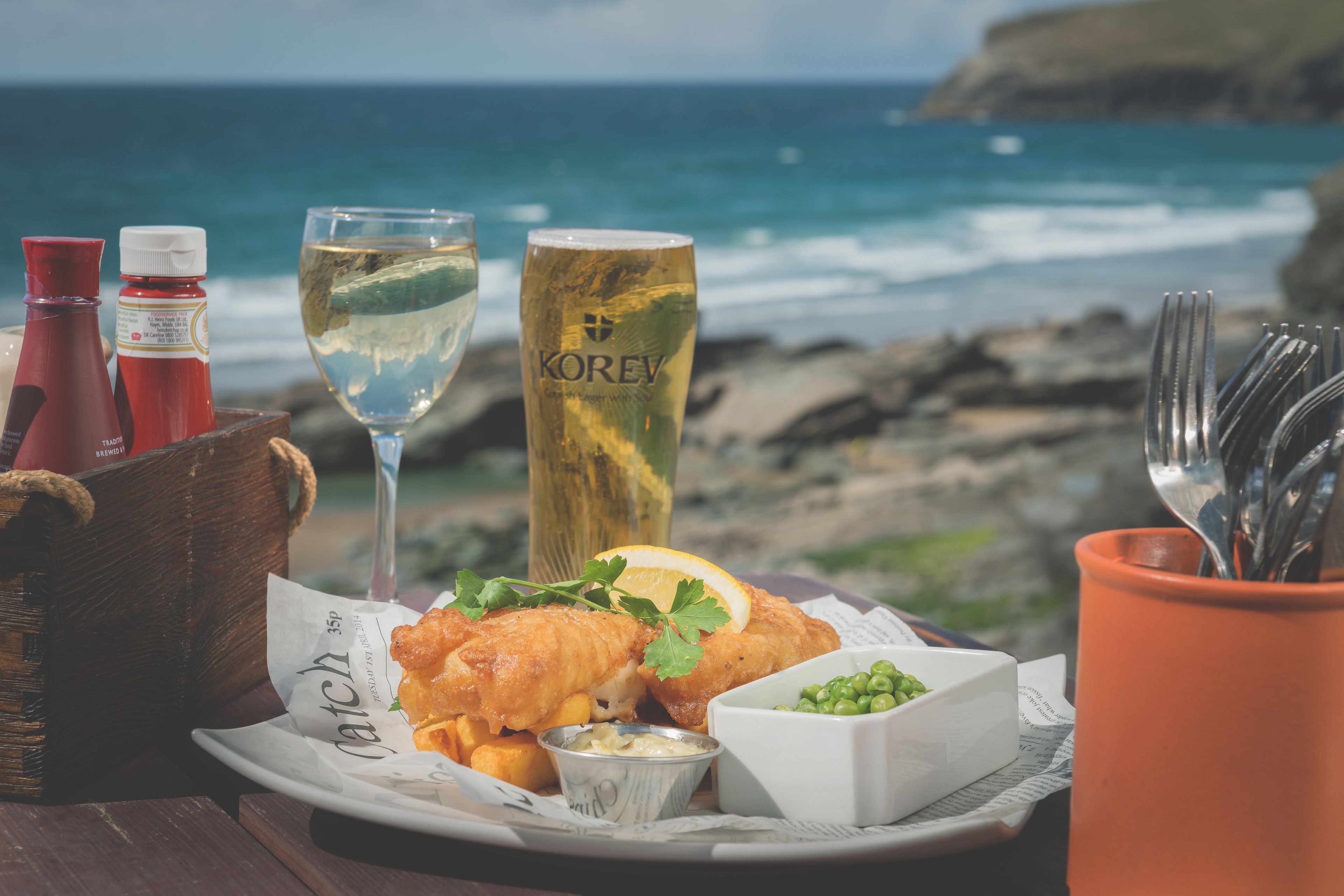 A seafood dish with a glass of white wine and a bottle of red sauce on a table by the sea.