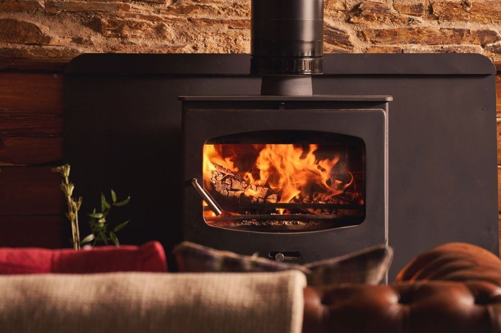 A wood-burning stove with a visible fire, set against a brick wall.