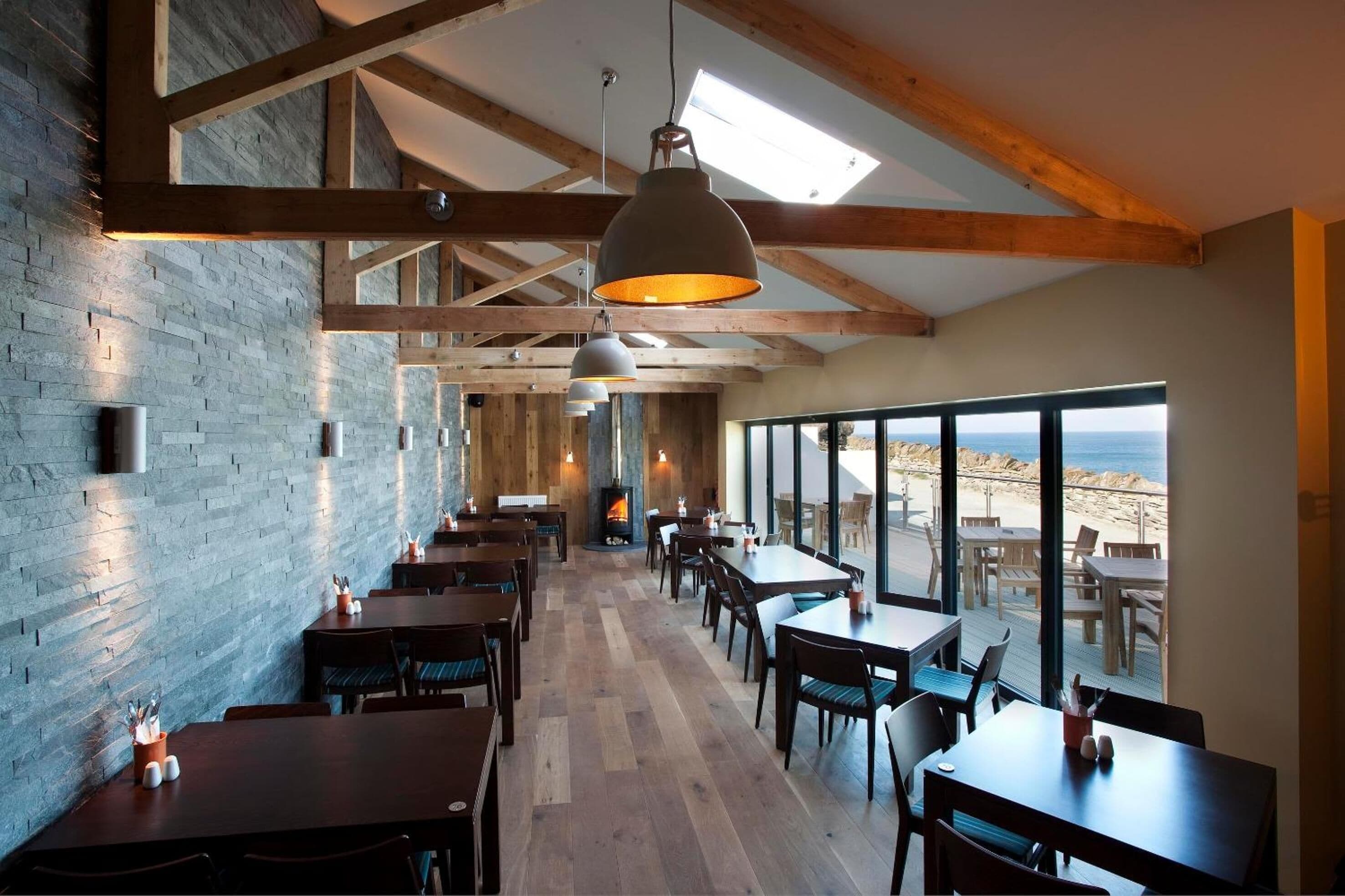Un restaurante con vigas de madera, paredes de ladrillo y ventanas amplias con vistas a la playa.