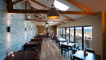 Un restaurante con vigas de madera, paredes de ladrillo y ventanas amplias con vistas a la playa.