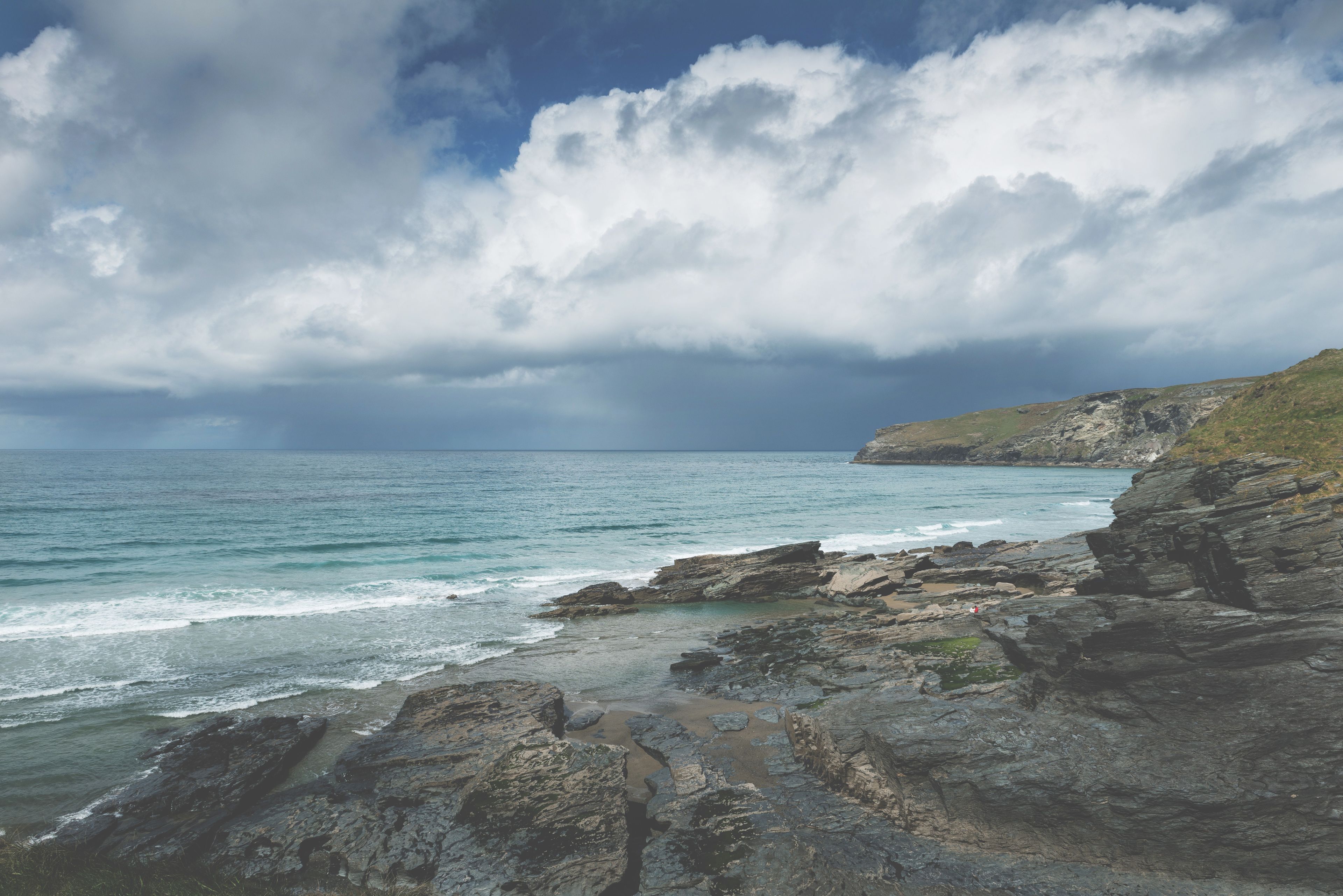 A coastal landscape with rocky terrain and a view of the sea under a cloudy sky.