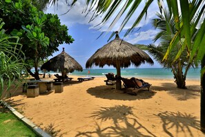 A beach with thatched umbrellas, lounge chairs, and a clear view of the ocean. - Sea Rock Villa (Induruwa)