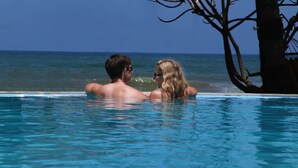A couple in a clear blue pool with a view of the ocean and a palm tree. - Sea Rock Villa (Induruwa)