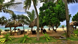 A beachside resort with thatched-roof structures, lounge chairs, and a clear view of the ocean. - Sea Rock Villa (Induruwa)