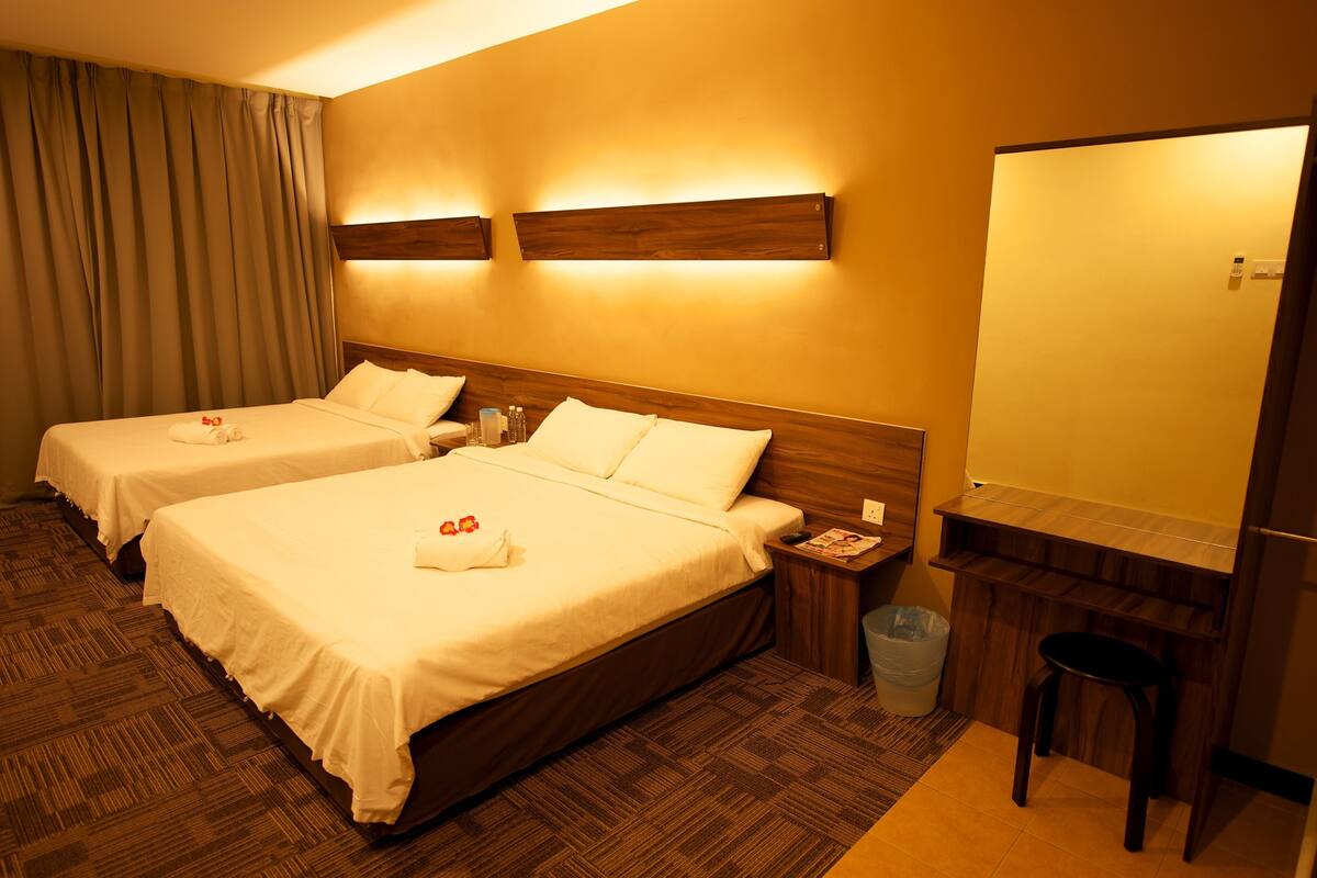Habitación de hotel con dos camas, un cabecero de madera, un escritorio pequeño con una silla, un cesto de basura y un espejo adosado a la pared.