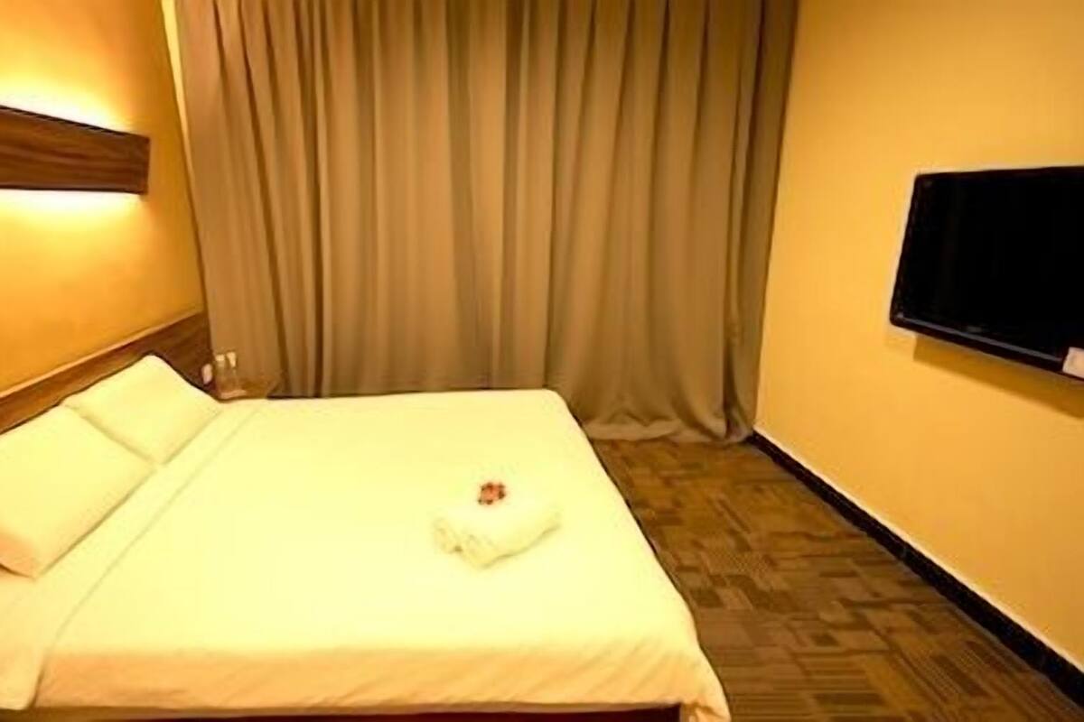 Una habitación de hotel con una cama bien hecha, un televisor de pantalla plana en la pared y un cabecero de madera.