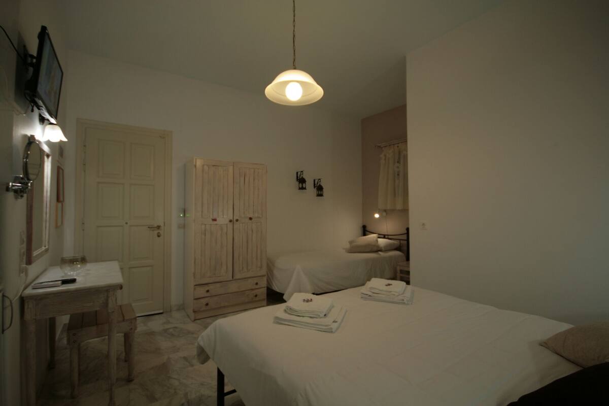 A bedroom with two beds, a desk, a wardrobe, and a hanging light fixture.