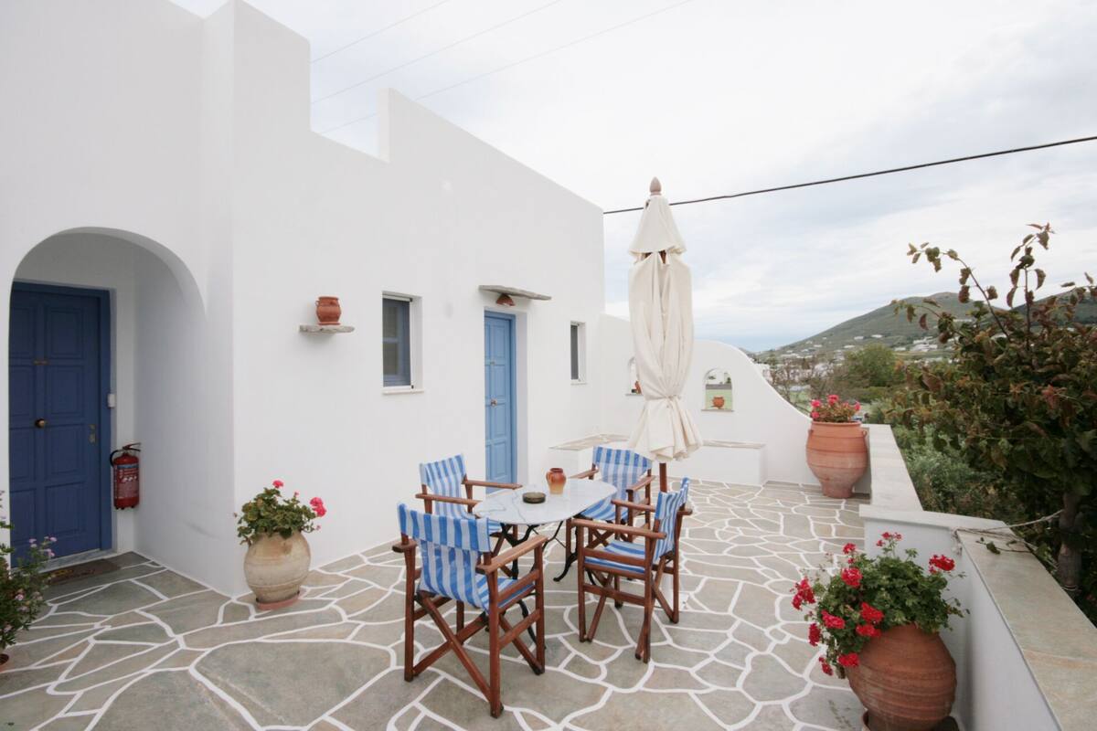 A white-walled outdoor seating area with blue doors, a table, and chairs.