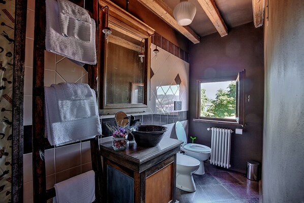 A bathroom with a wooden vanity, a large mirror, a sink, two toilets, and a window with a view of greenery.