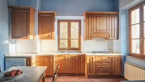 A kitchen with wooden cabinets, a sink, a stove, and a window. - Palazzo Gatteschi (Poppi)