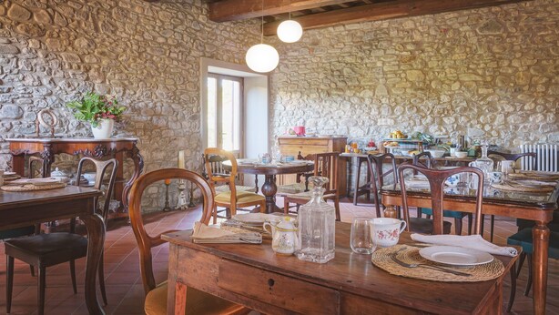A rustic dining area with stone walls, wooden furniture, and a stone fireplace. - Palazzo Gatteschi (Poppi)