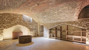 A stone-walled room with wooden shelves and a large barrel. - Palazzo Gatteschi (Poppi)
