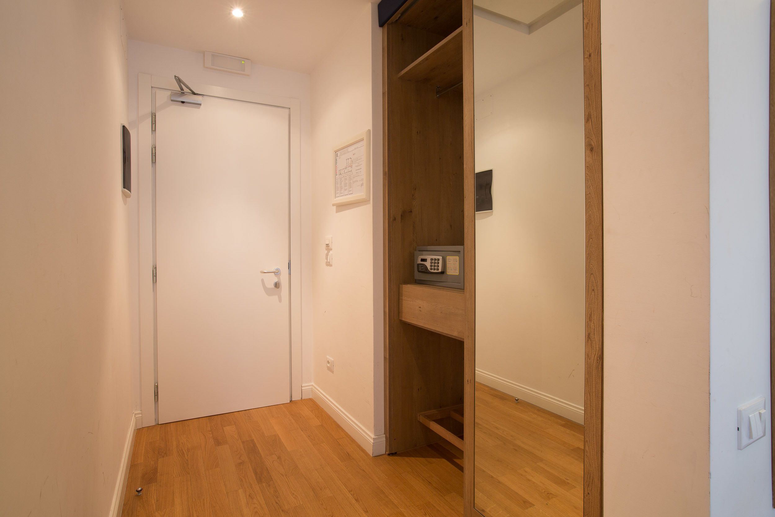 A hallway with a wooden floor, a white door, and a wooden closet with a shelf.