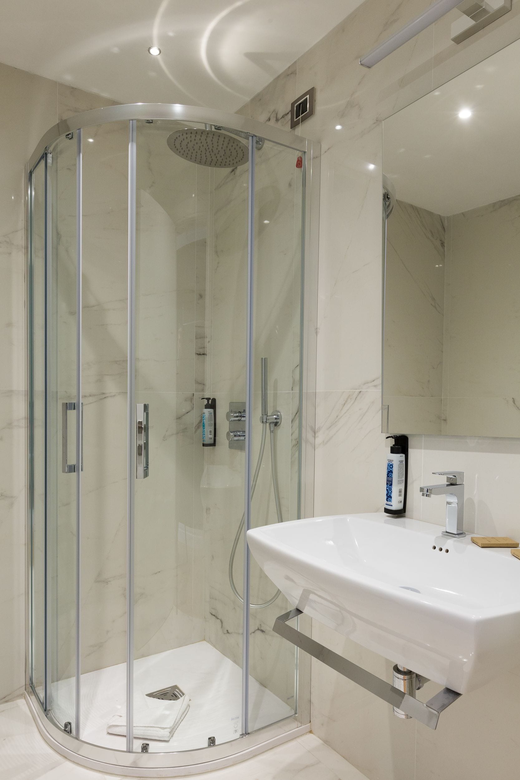 Un baño moderno con ducha envuelta en vidrio, un lavabo blanco y un espejo grande.