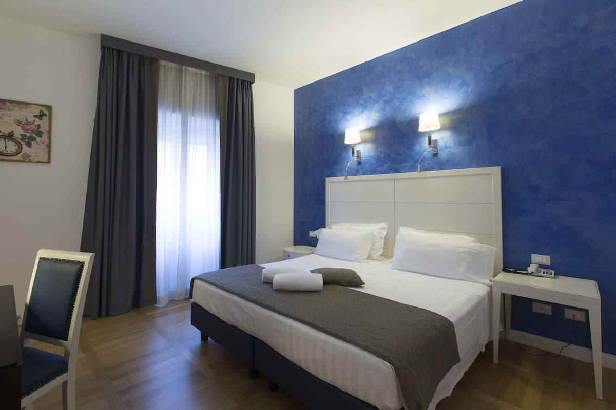 A hotel room with a large bed, a chair, a nightstand, and a wall clock.
