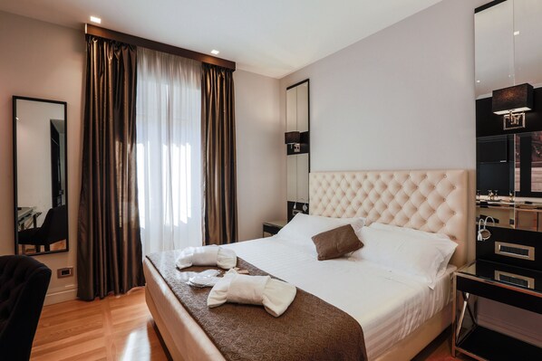 Habitación de hotel con una cama grande, una mesita de noche, un espejo, un armario y una ventana con cortinas.