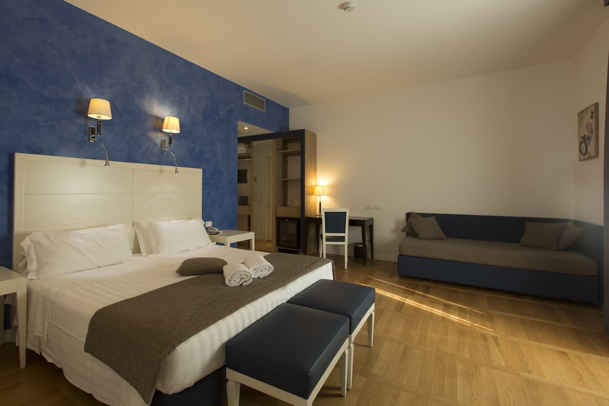 A bedroom with a large bed, bedside tables, a bench, a sofa, and a desk with a chair.