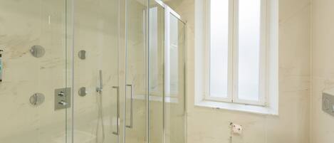 A modern bathroom with a glass-enclosed shower, a toilet, and a window providing natural light.