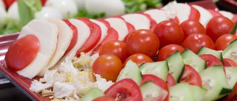 A buffet with various food items including sliced tomatoes, cucumbers, and cheese.
