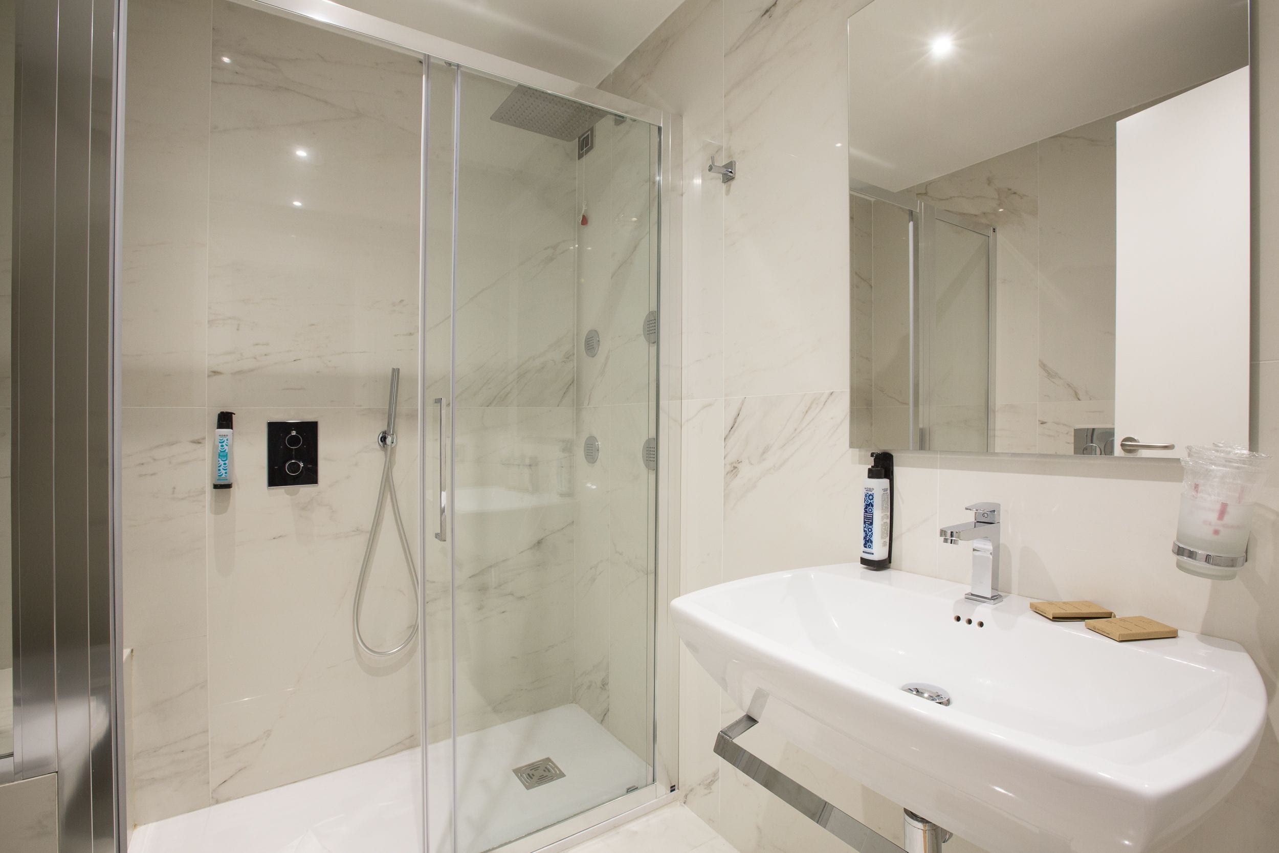 Une salle de bain moderne avec une douche à parois de verre, un lavabo blanc et un miroir.