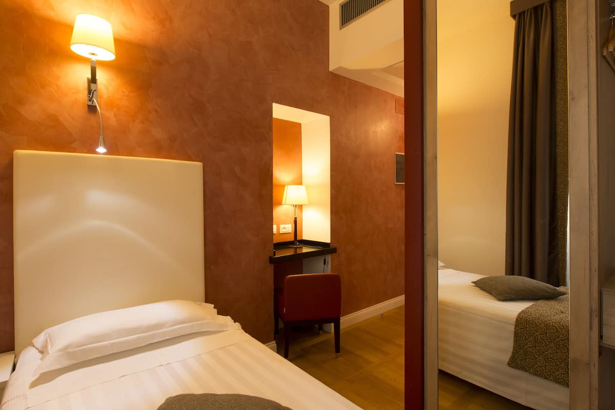 A hotel room with a bed, a desk, a chair, and a mirror.