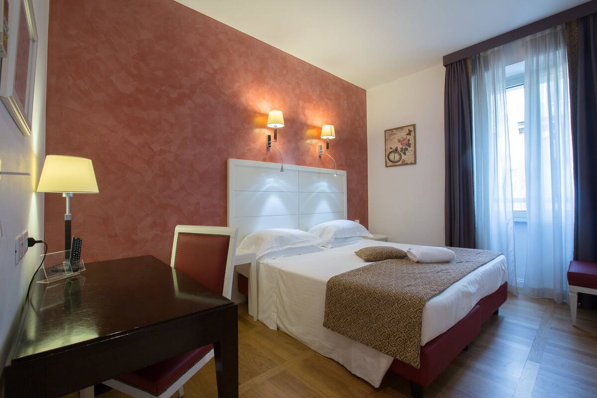 A hotel room with a bed, bedside tables, a desk, and a chair.