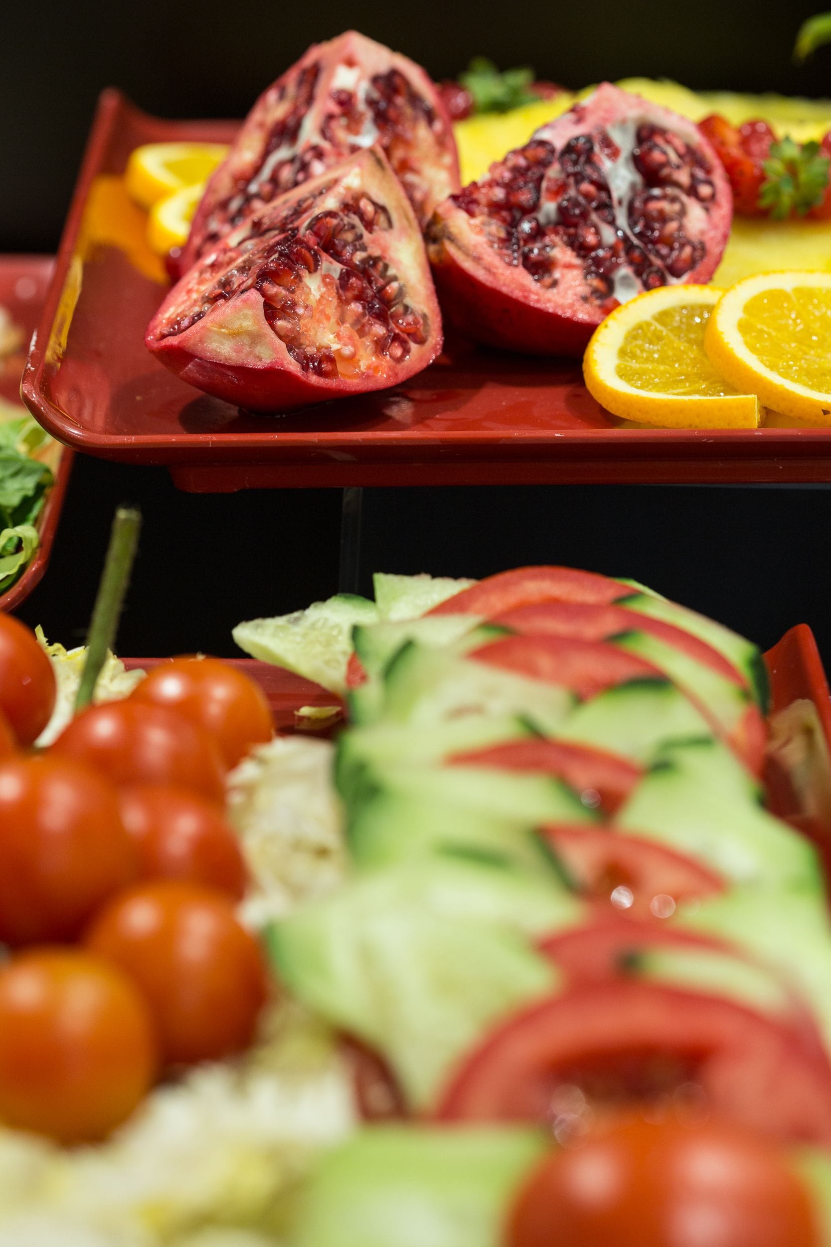 Una selezione di frutta e verdura fresca, tra cui melograni a metà, spicchi d'arancia, pomodorini ciliegino e fette di cetriolo, disposti su un vassoio.