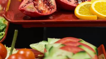 Una selezione di frutta e verdura fresca, tra cui melograni a metà, spicchi d'arancia, pomodorini ciliegino e fette di cetriolo, disposti su un vassoio.
