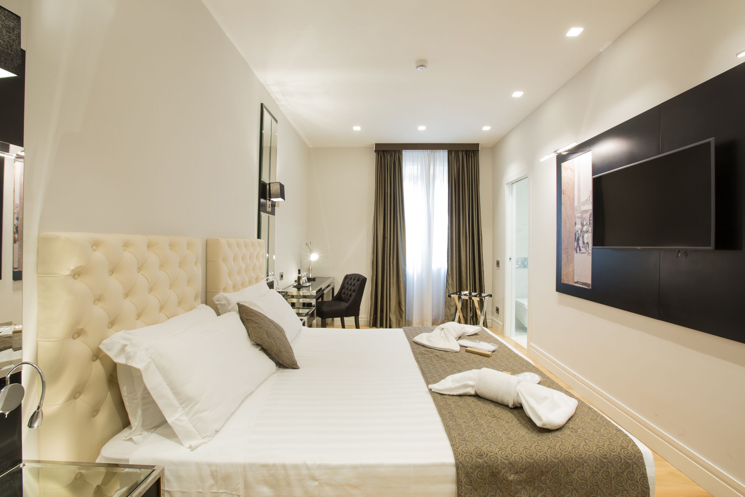 A hotel room with a large bed, a desk, a chair, and a television on the wall.