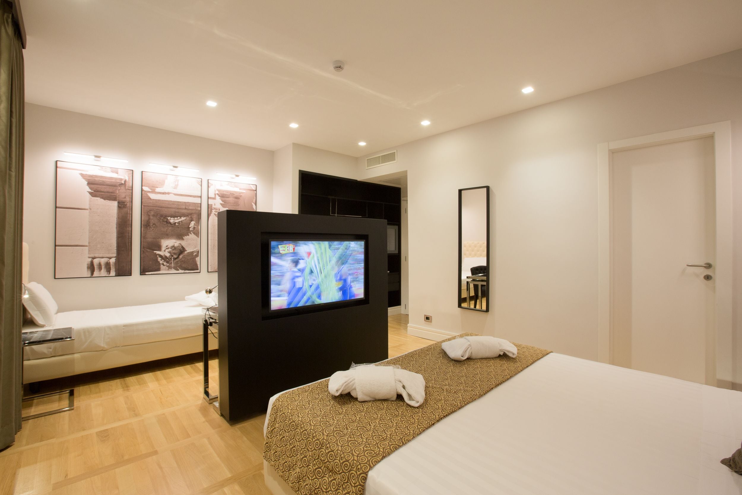 Ein modernes Hotelzimmer mit einem Bett, einem Fernseher, einer Schlafcouch und einem Spiegel.