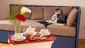 Ein Zimmer mit einer Couch, einem kleinen Tisch mit einer Essschale, einer Blumenvase und einem Buch.