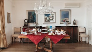 A dining room with a wooden table set for a meal, surrounded by chairs, with a chandelier above. - B&B Triskéles (Agrigento)