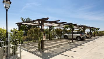 Uma área de estacionamento coberta com estrutura de pérgola, um poste de luz e um caminho pavimentado.