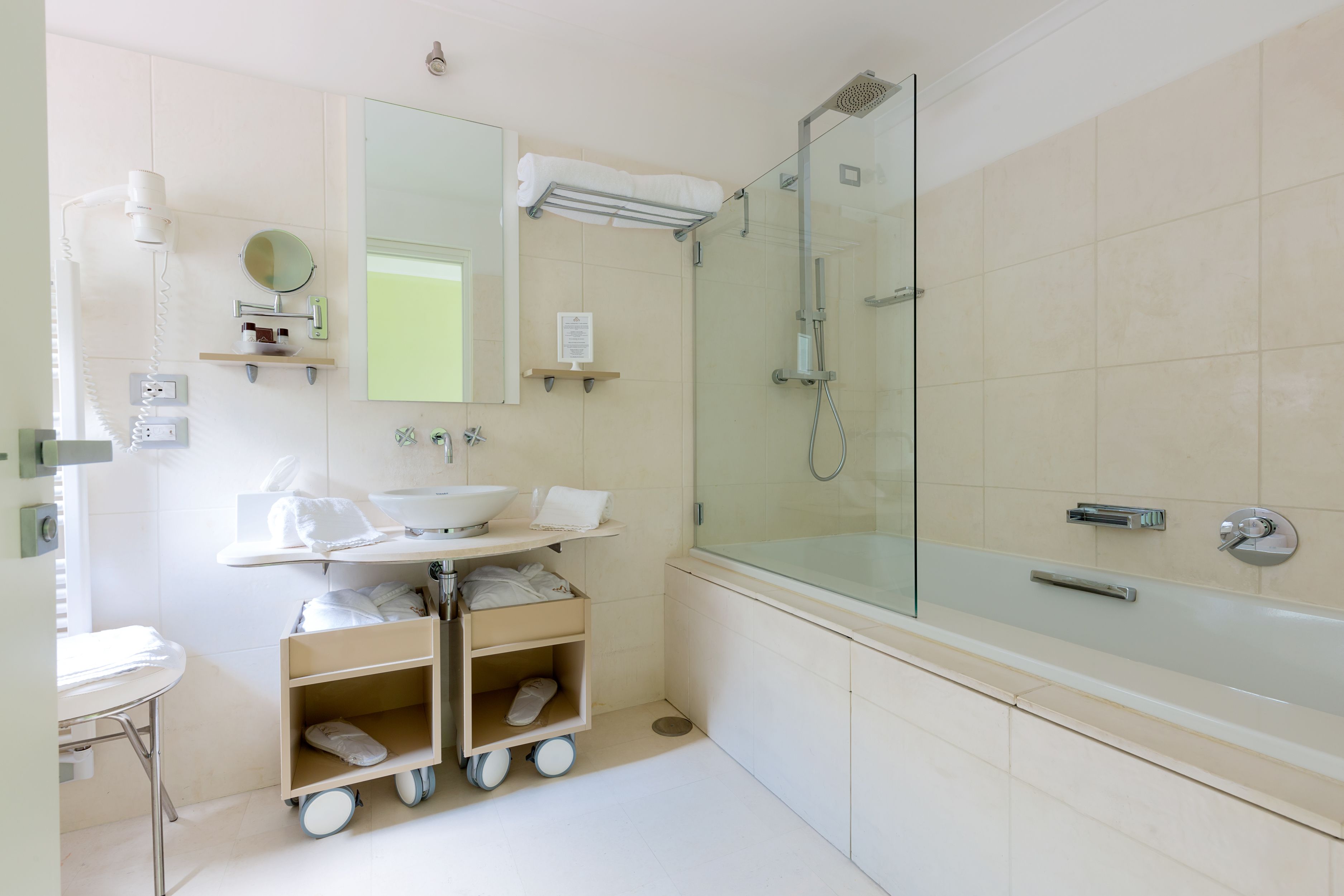 Ein modernes Badezimmer mit einer Glaskabine zur Dusche, einem Waschbecken mit Spiegel und einem Tablett für Pflegeprodukte.