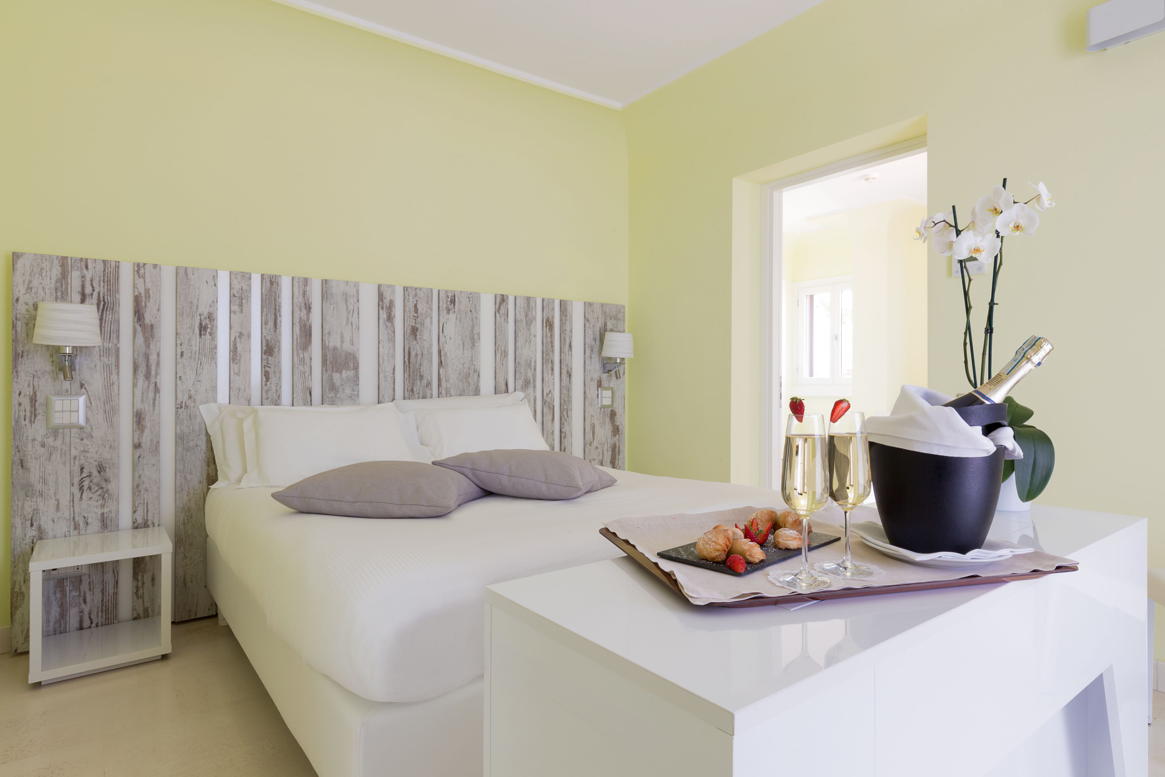 Une chambre d’hôtel avec un lit, une table de chevet et un bureau sur lequel se trouvent un seau et des fleurs.