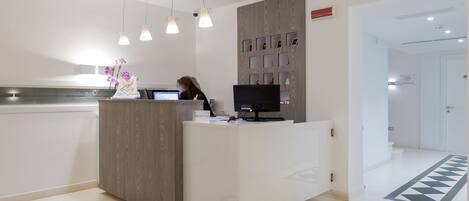A reception desk with a computer, a person at the desk, and a decorative vase with flowers.