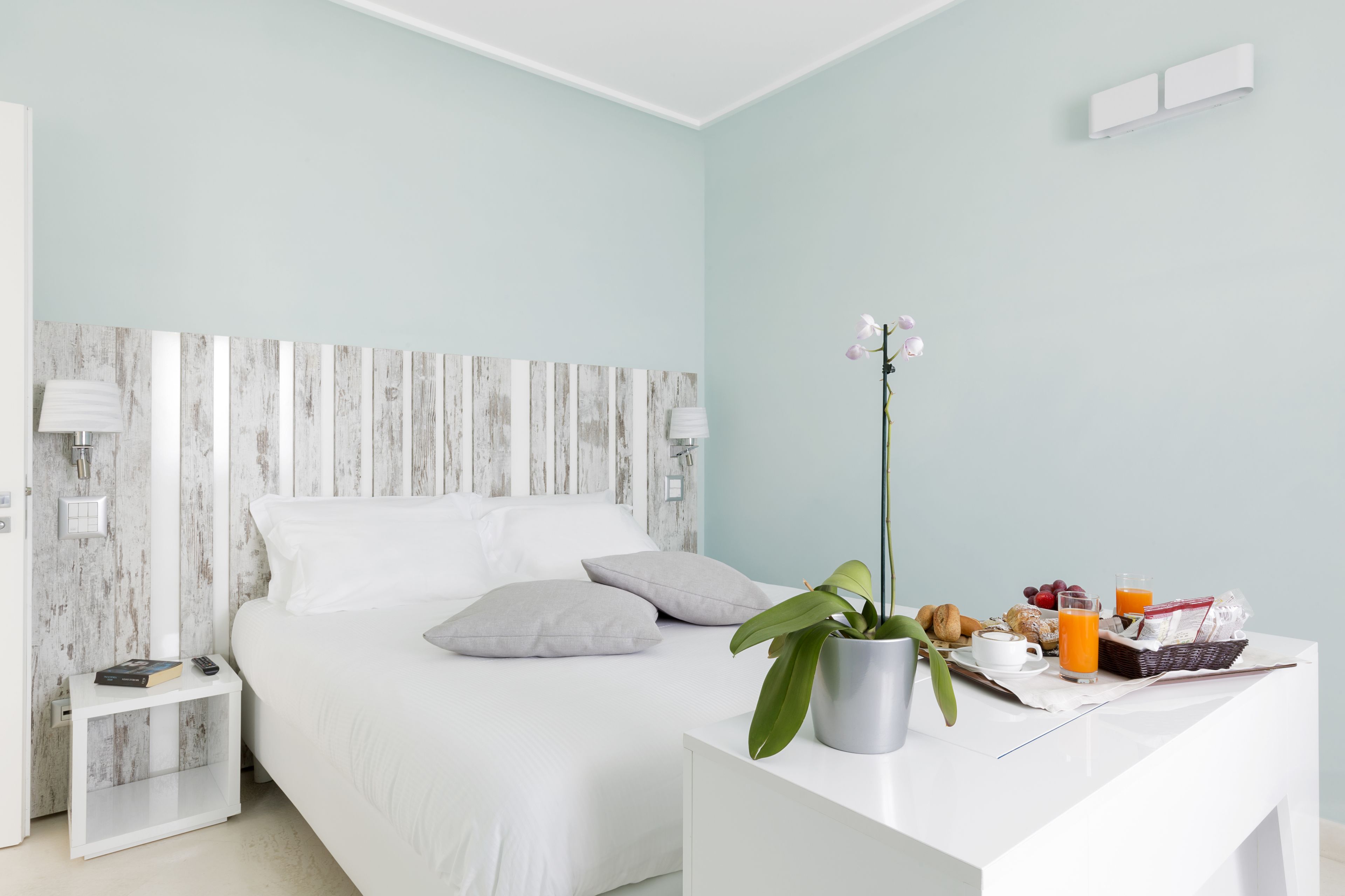 A modern bedroom with a bed, bedside tables, a nightstand, a potted plant, and a breakfast tray with fruits and juice.