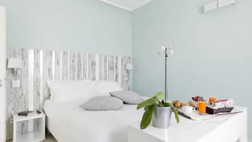 A modern bedroom with a bed, bedside tables, a nightstand, a potted plant, and a breakfast tray with fruits and juice.