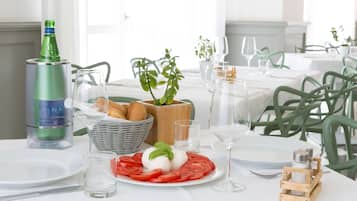 A dining table set with a plate of tomato and mozzarella, a bottle of water, a glass, and a small wooden salt shaker.