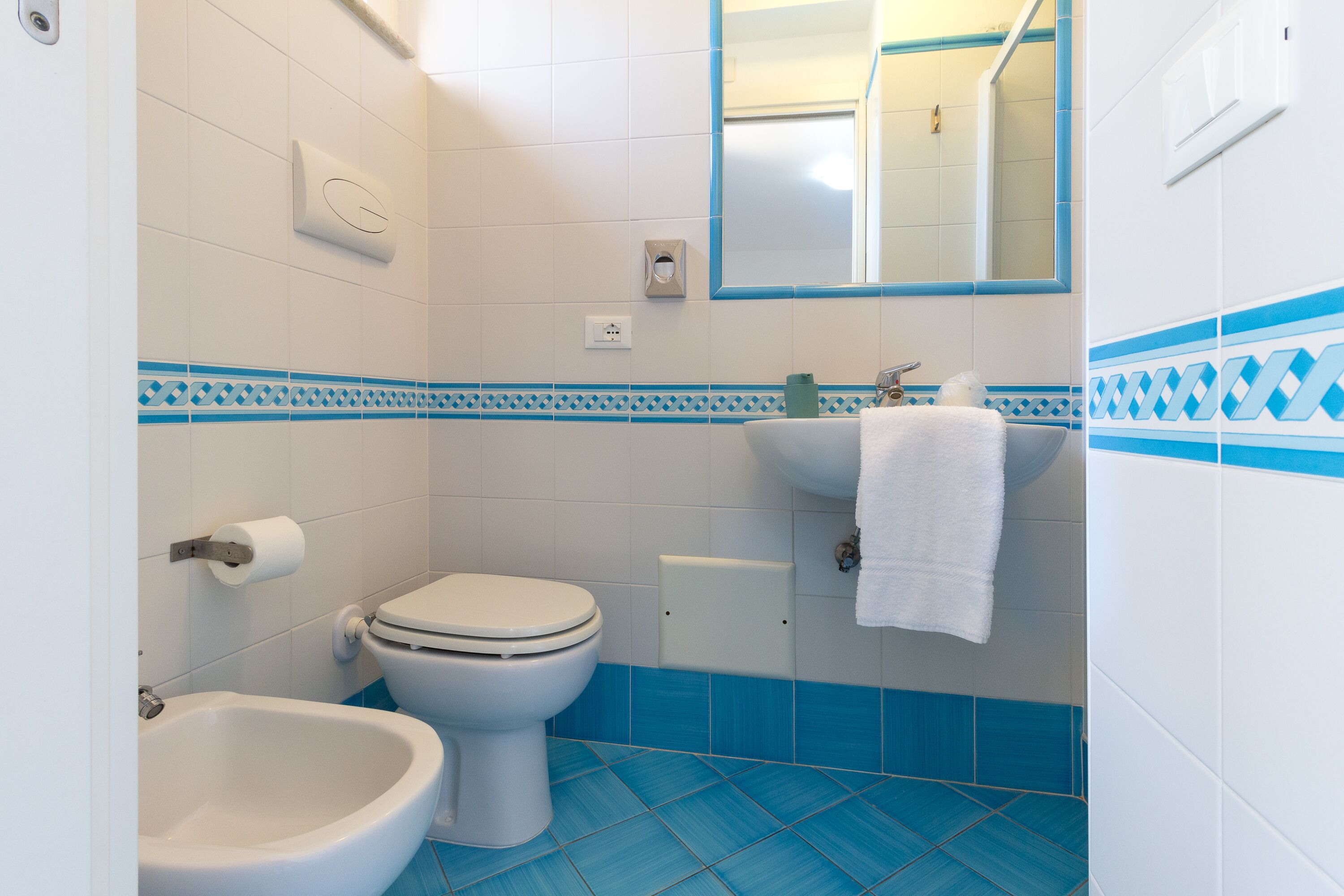 A bathroom with a toilet, bidet, and sink, featuring blue and white tiles.