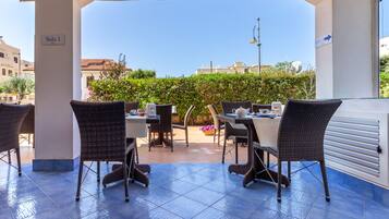 Une terrasse extérieure avec des meubles en osier et un sol carrelé, portant l’inscription « Salle 1 ».