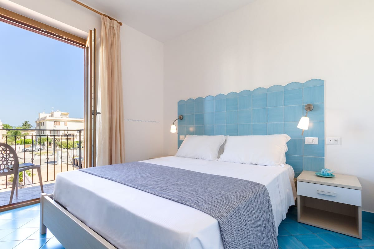 Ein Hotelzimmer mit Bett, Nachttisch, Stuhl und Blick ins Freie.