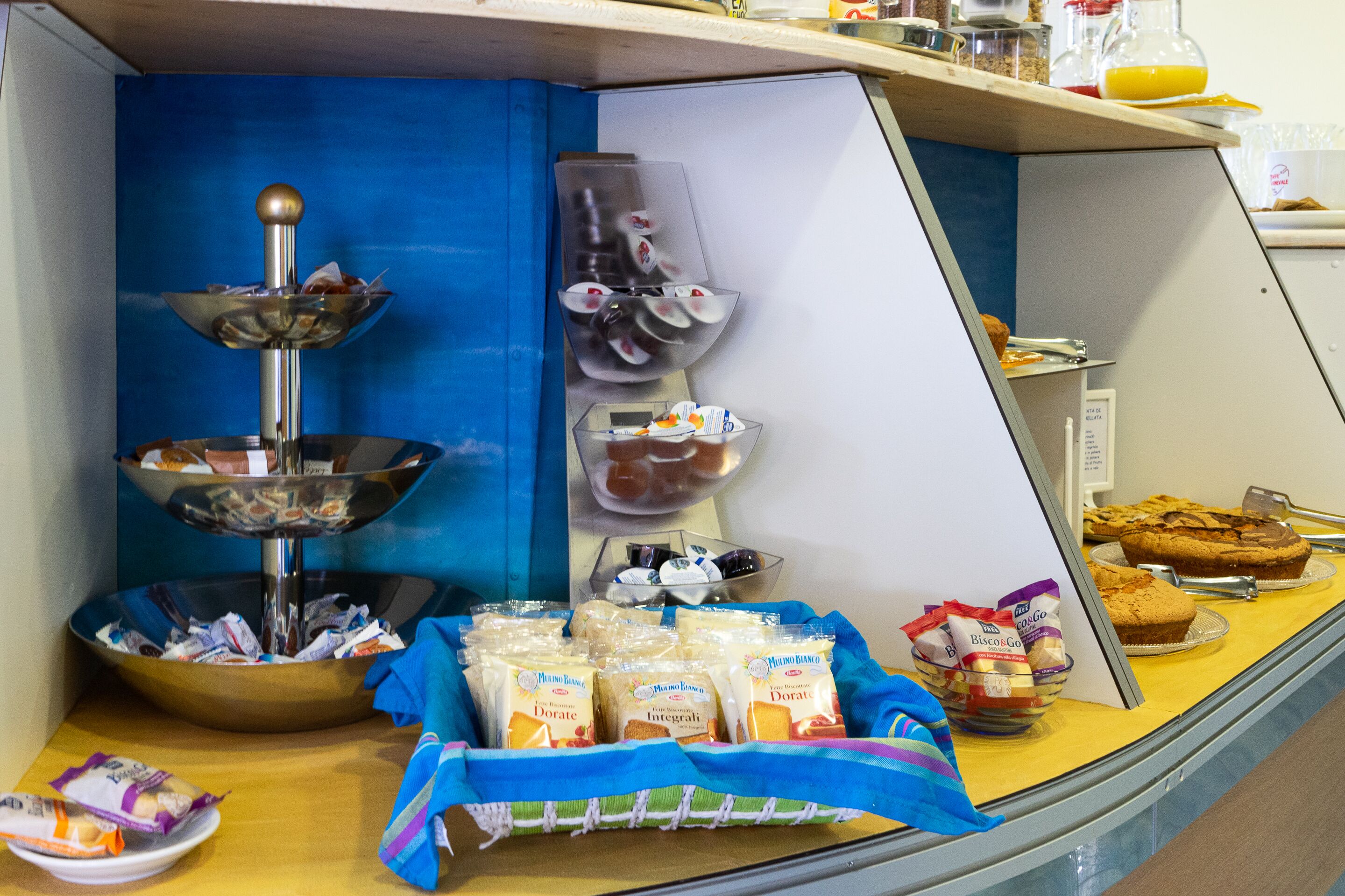 A buffet area with a variety of food items, including Dorate and Bisco Go, arranged on a yellow tablecloth.