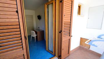 Una habitación con puerta de madera que da a un baño, un escritorio pequeño con silla, y suelo de baldosas.