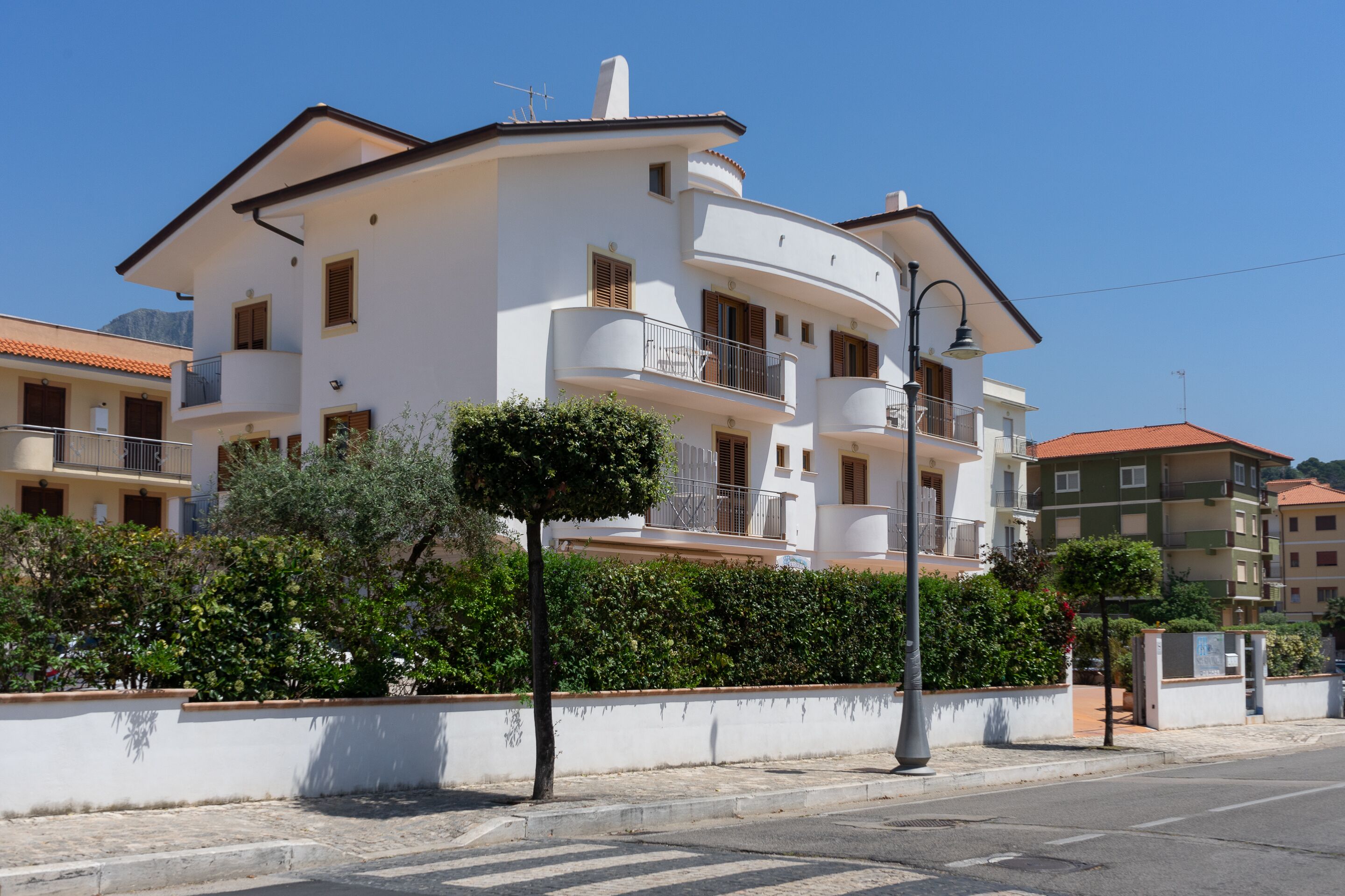 Un edifici residencial de diversos pisos amb balcons, cel blau clar i una tanca al primer pla.