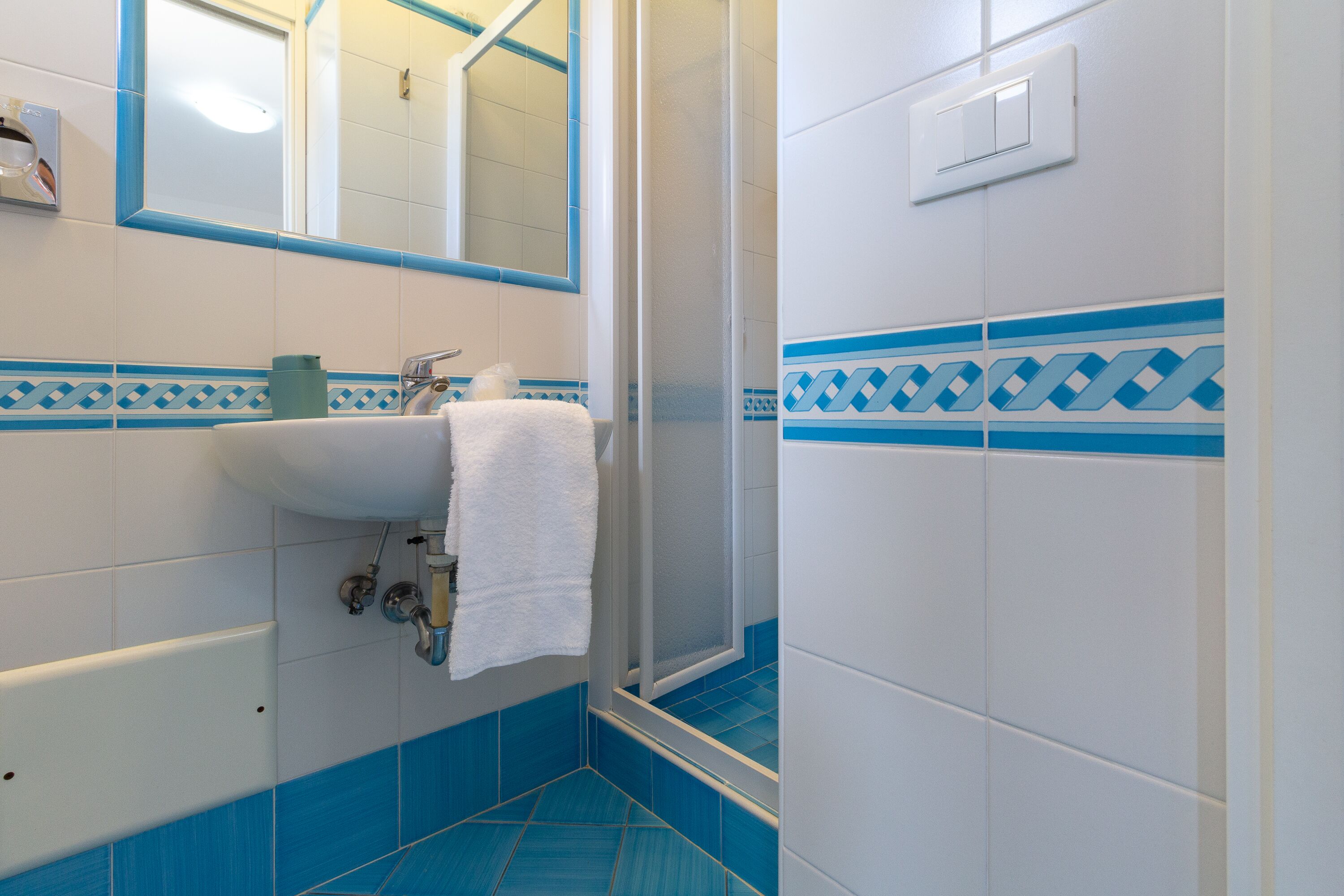 A bathroom with a white sink, blue tiles, a mirror, and a shower area.