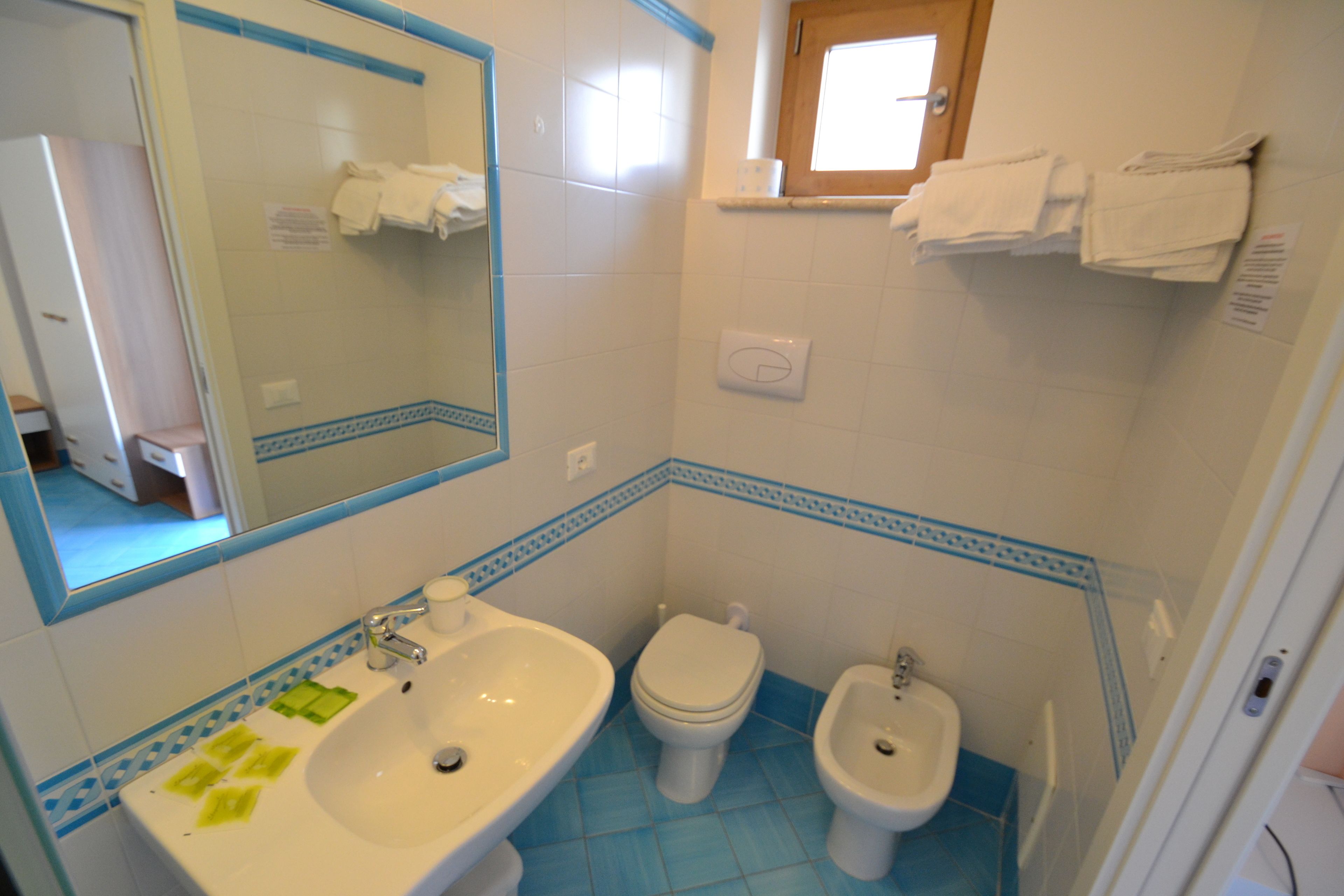 A bathroom with a sink, toilet, and bidet. There is a mirror above the sink and a window above the toilet.