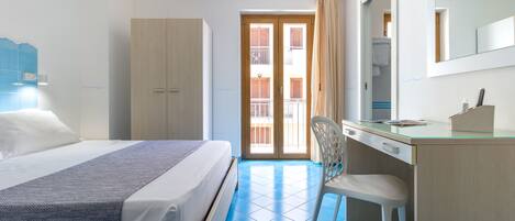 A hotel room with a bed, a desk, a chair, a wardrobe, and a balcony with a view of the building.